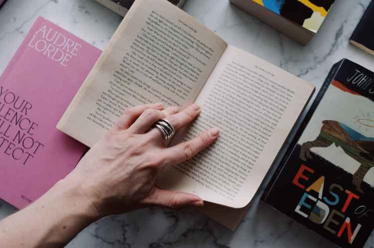 anonymous crop person reading book on marble surface with other books